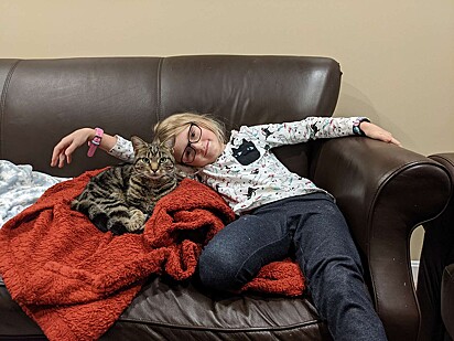 A gatinha está deitada no sofá com uma das crianças da família.