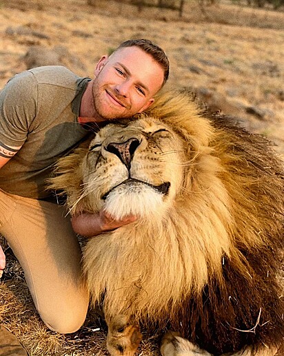 Outra foto do rapaz sorrindo ao lado de um leão.