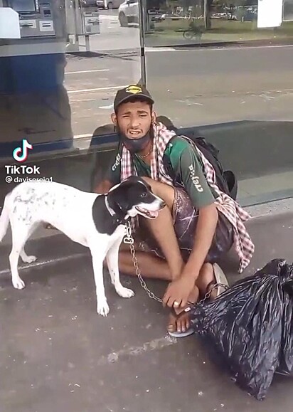 Homem e cadela estão em frente a um banco.