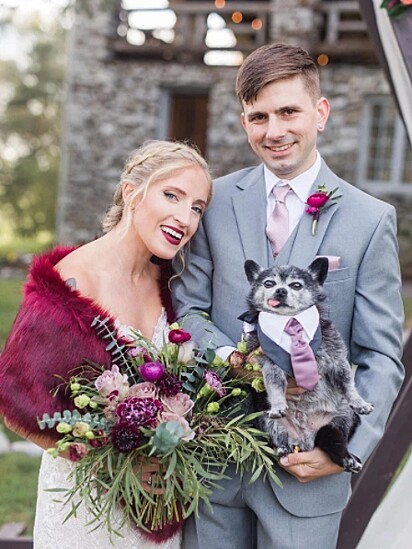 Os noivos estão posando para a foto com o cãozinho.