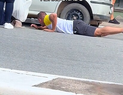 O homem se deitou no chão para pegar a cachorrinha que estava debaixo do carro estacionado.