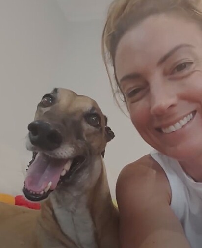 A cachorrinha da raça galgo, Poppy, sorrindo ao lado de sua tutora, Emma.