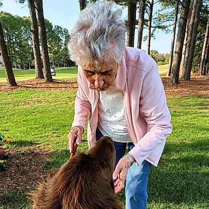 Barbara se abaixa para o Chewy durante o plantio Com a bengala numa das mãos, ela se inclina para o cachorro no meio do trabalho no canteiro